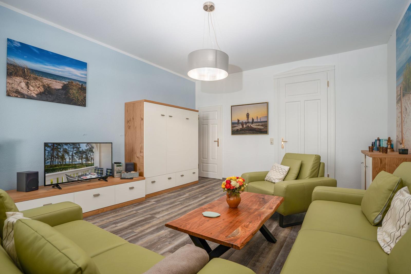 Living room with green chairs, wooden table, and TV on light blue wall.