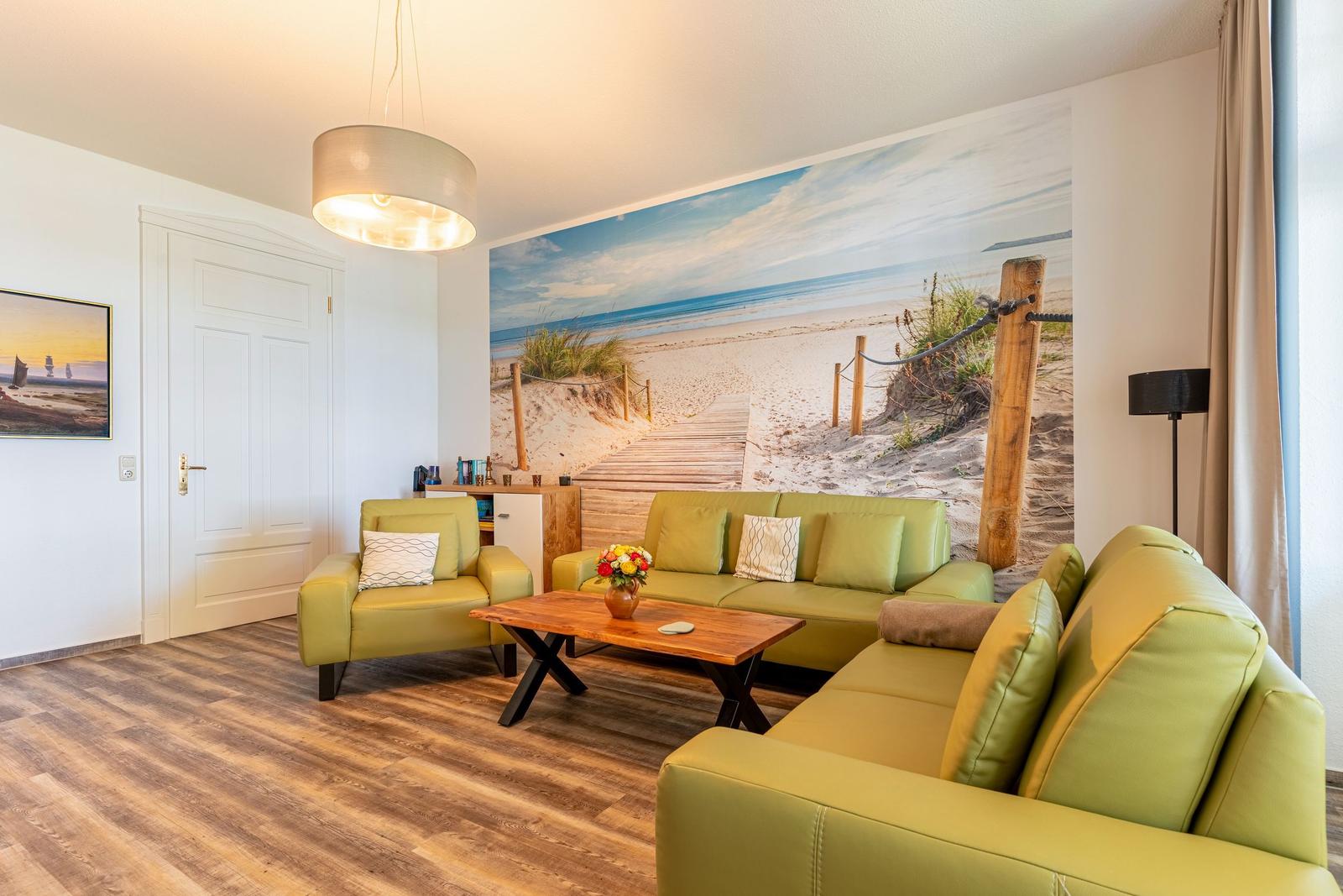 Living room with green sofas, wooden table, and beach mural on the wall.
