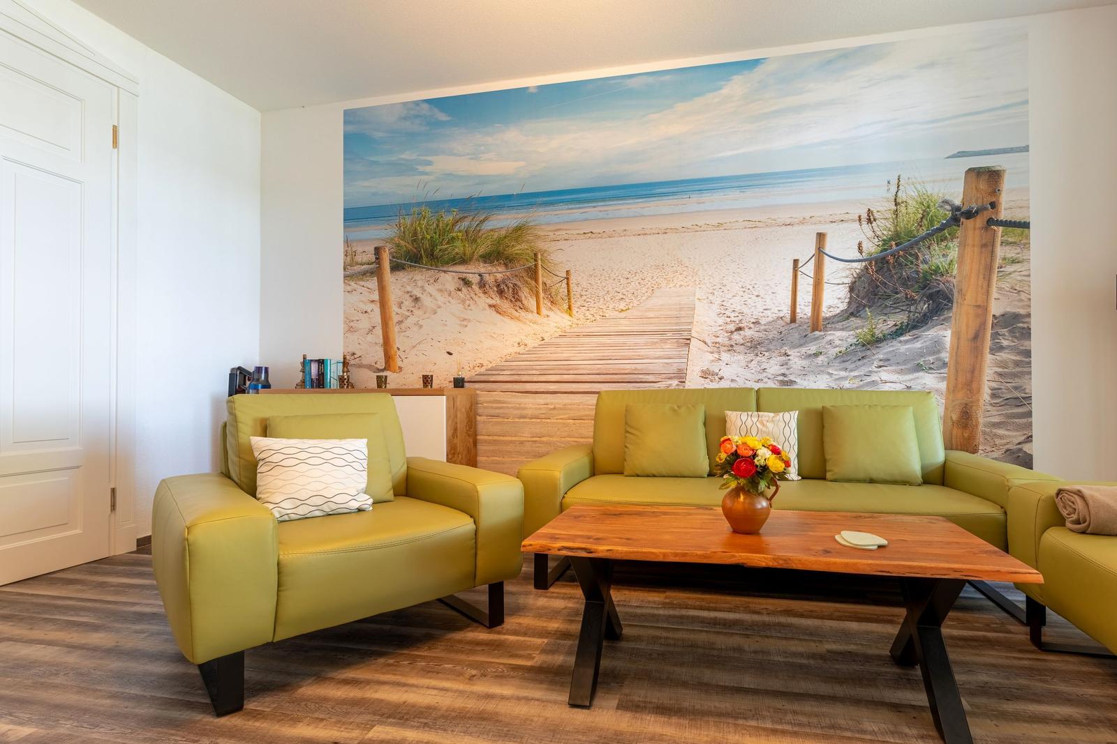 Living room with green seating and beach mural on the wall.