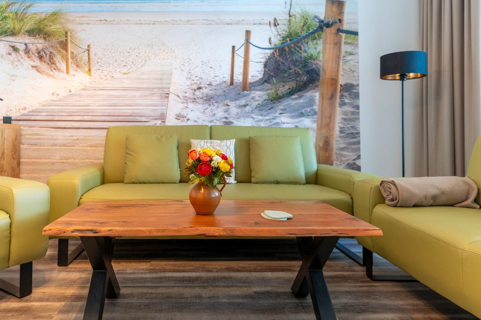 A living room with green sofa, wooden table, and beach mural on the wall.