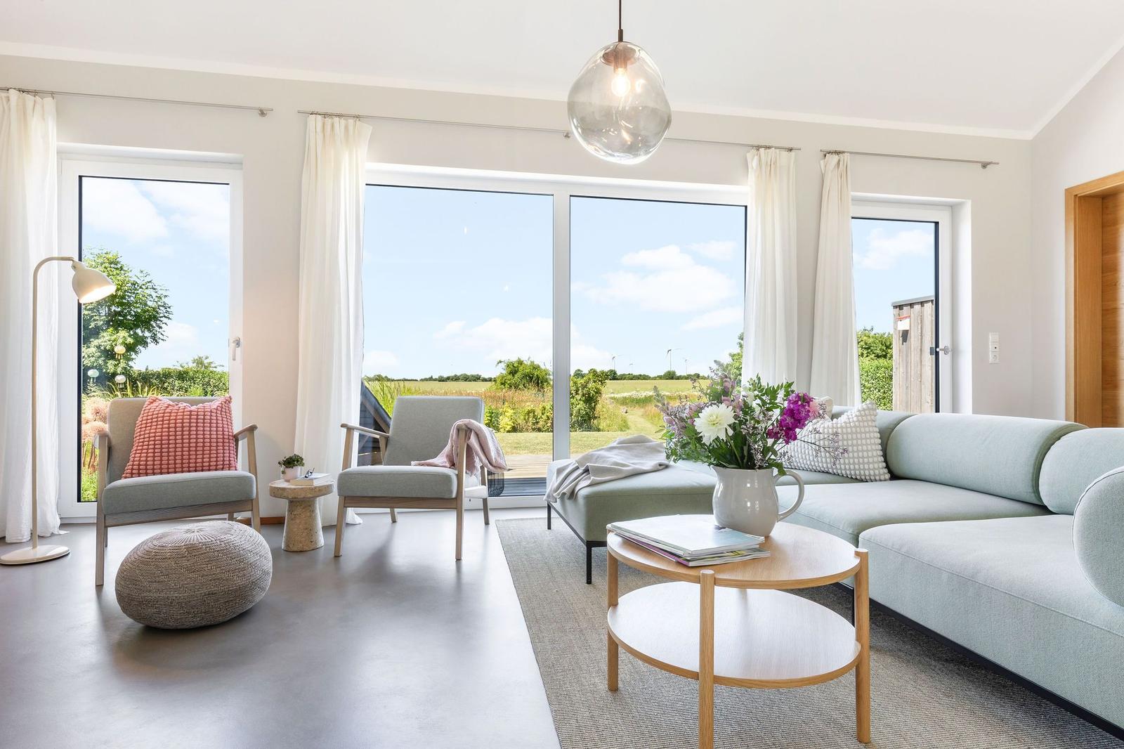 Wohnzimmer mit Sofa, Sitzgelegenheiten und Blick auf grüne Landschaft.