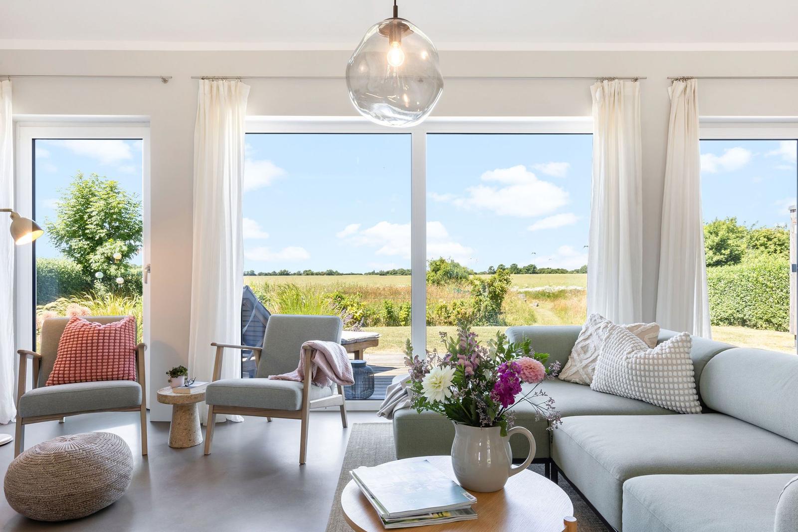 Lichter Wohnzimmer mit Sofa, Sesseln und Blick auf Felder.