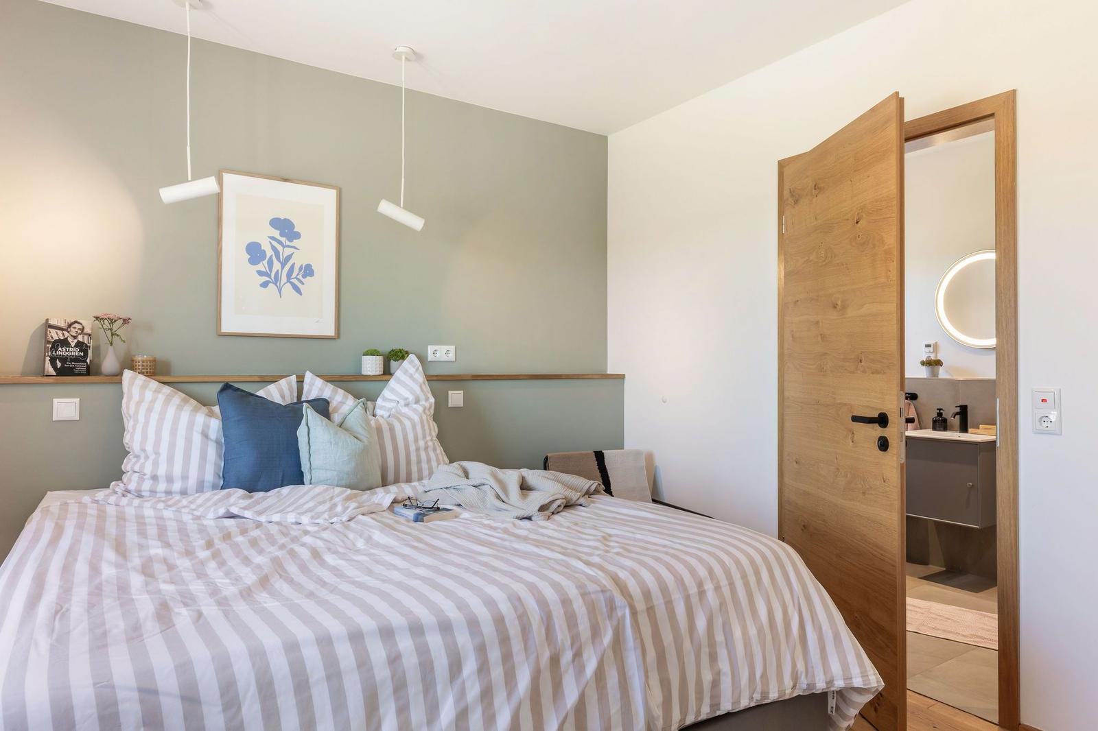 Schlafzimmer mit Bett, Wandbild und offener Tür zum Badezimmer.