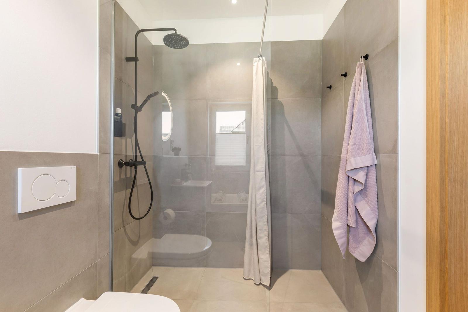 Dusche mit Duschbrause, Toilette und Handtuch an Wand
