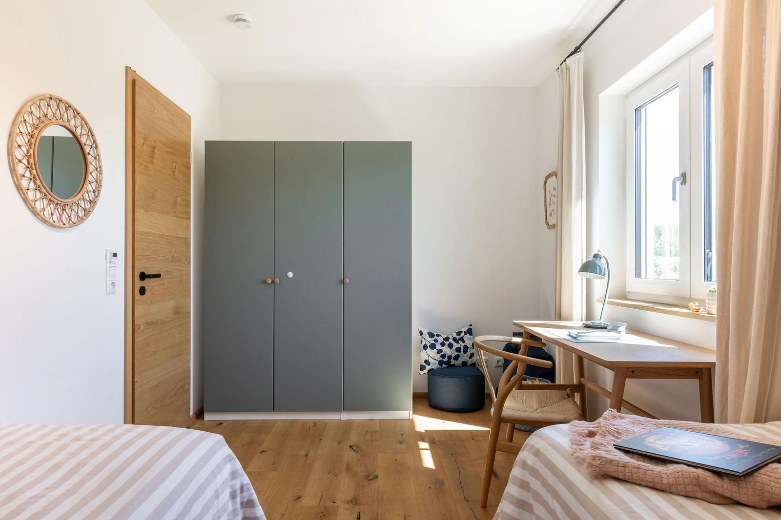 Schlafzimmer mit Doppelbett, Kleiderschrank und Schreibtisch am Fenster.