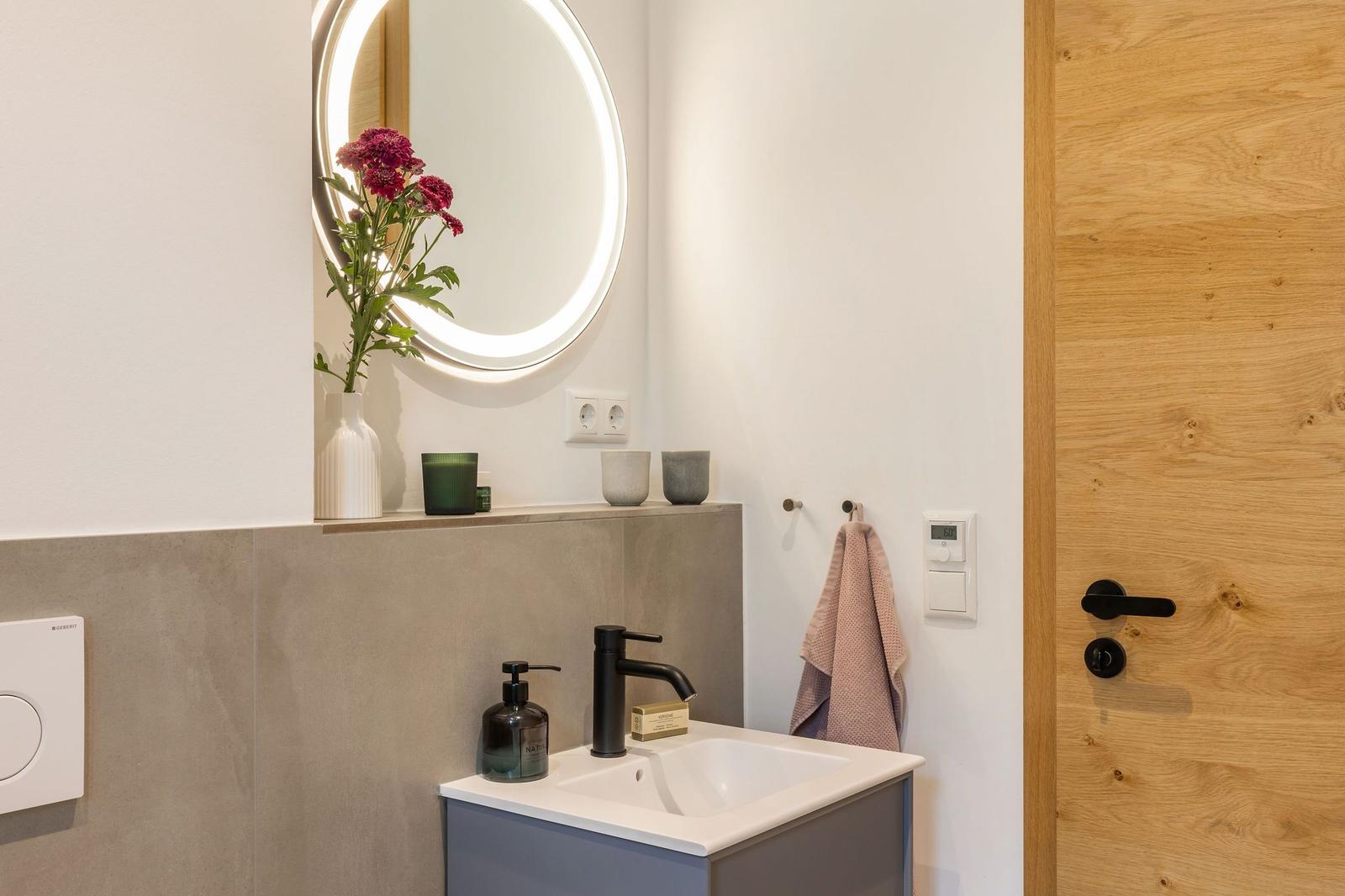 Badezimmer mit Waschbecken, Spiegel und Holztür.