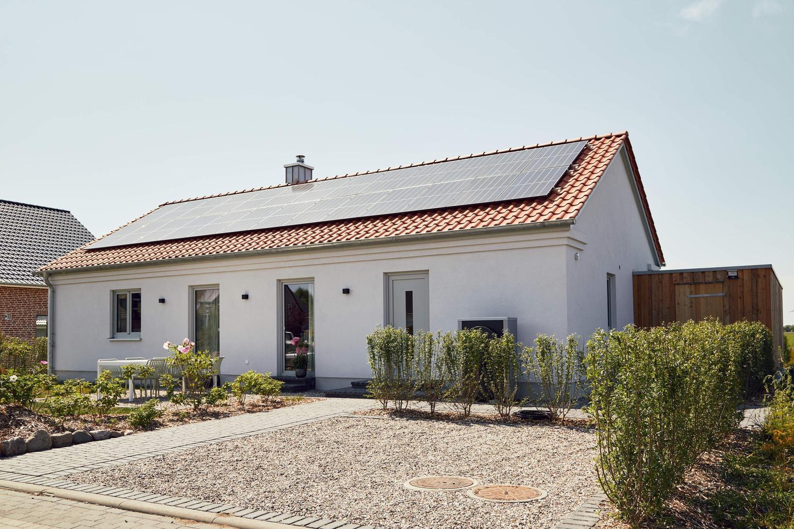 Moderne Villa mit Solaranlage, Terrasse und gepflastertem Hof. Grünflächen und Hecken umgeben das Haus.