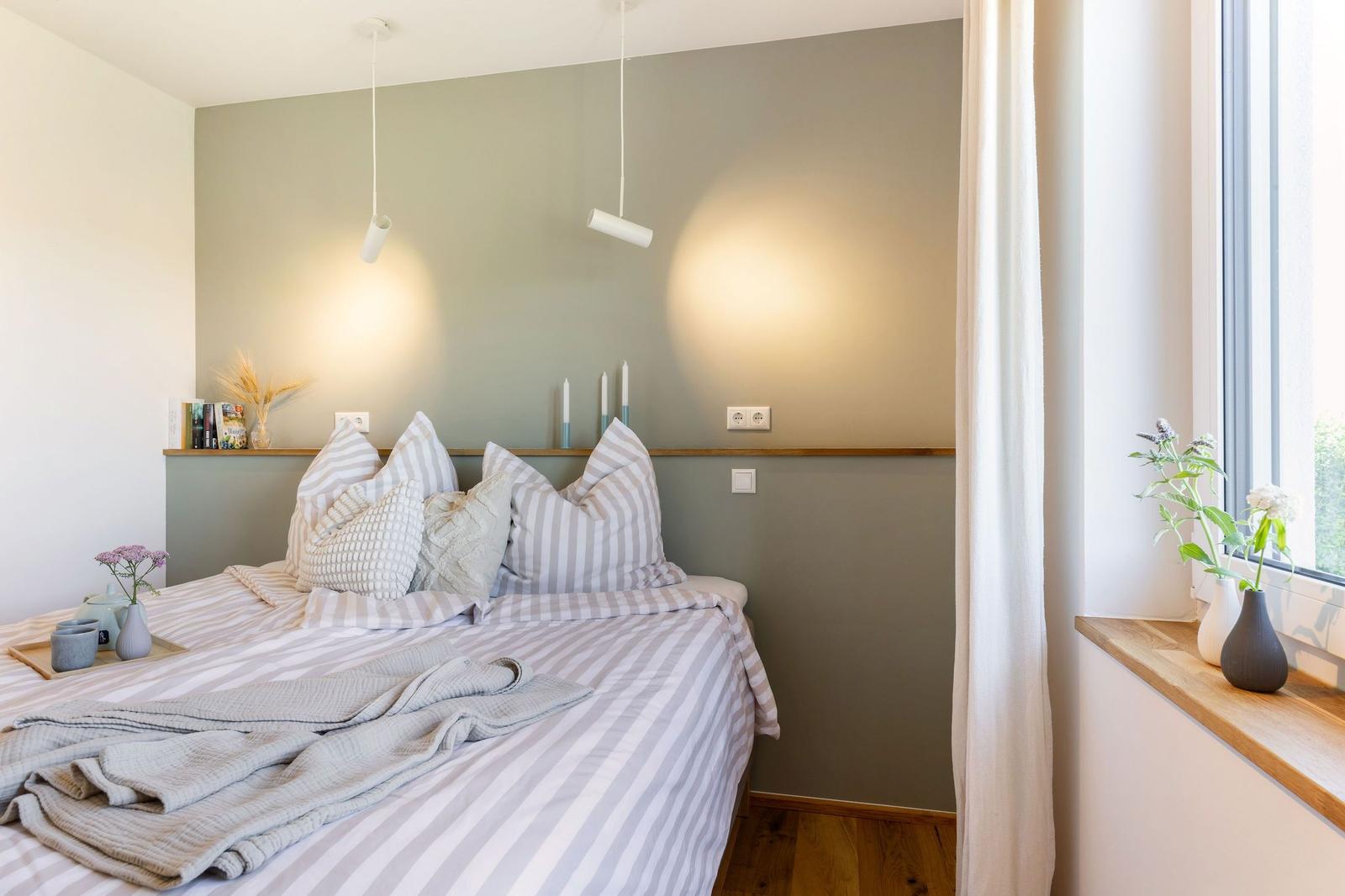 Schlafzimmer mit Bett, Fenster und moderner Beleuchtung.