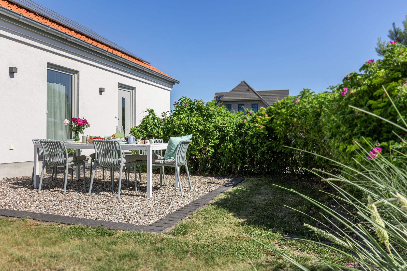 Terrasse mit Tisch und Stühlen vor weißem Haus mit rotem Dach