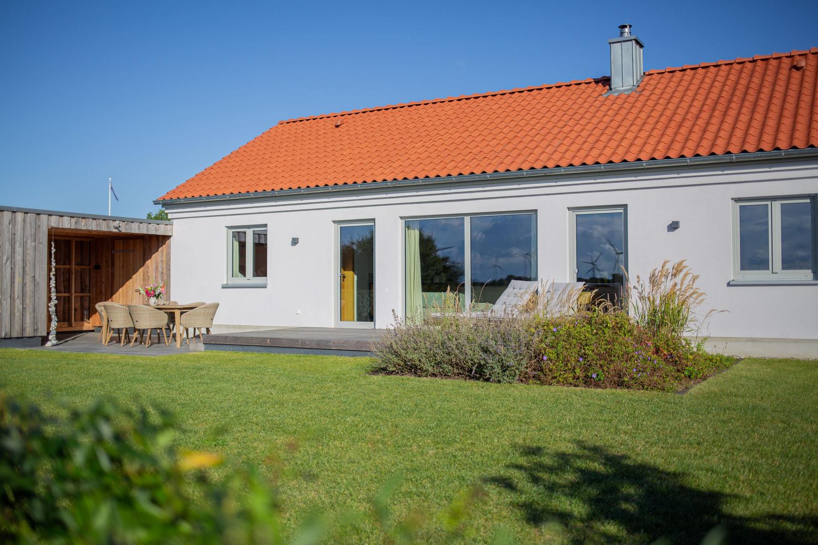 Wohnhaus mit Terrasse, Garten und Holzsauna. Große Fenster und roter Dachziegel.