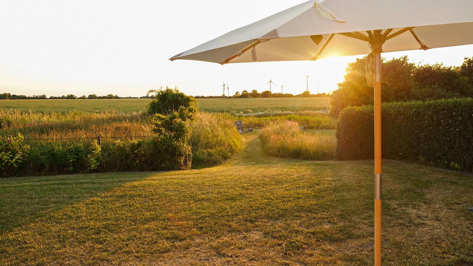 Garten mit Sonnenschirm, Feldweg und Windkraftanlagen im Hintergrund.