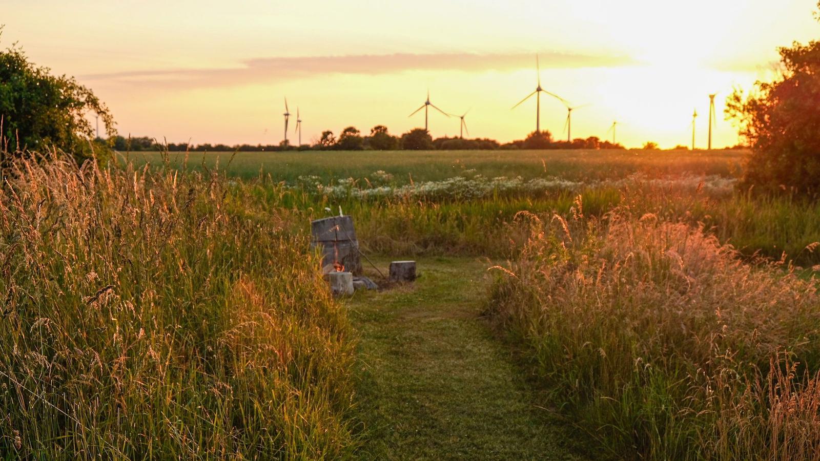 Weg durch Grasland mit Feuerstelle und Windkraftanlagen im Sonnenuntergang.