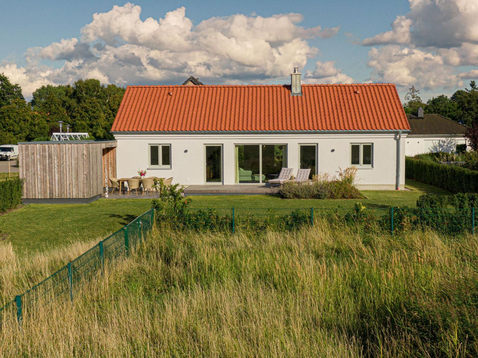Moderne Villa mit rotem Dach, Terrasse und Garten. Holzhaus nebenan.