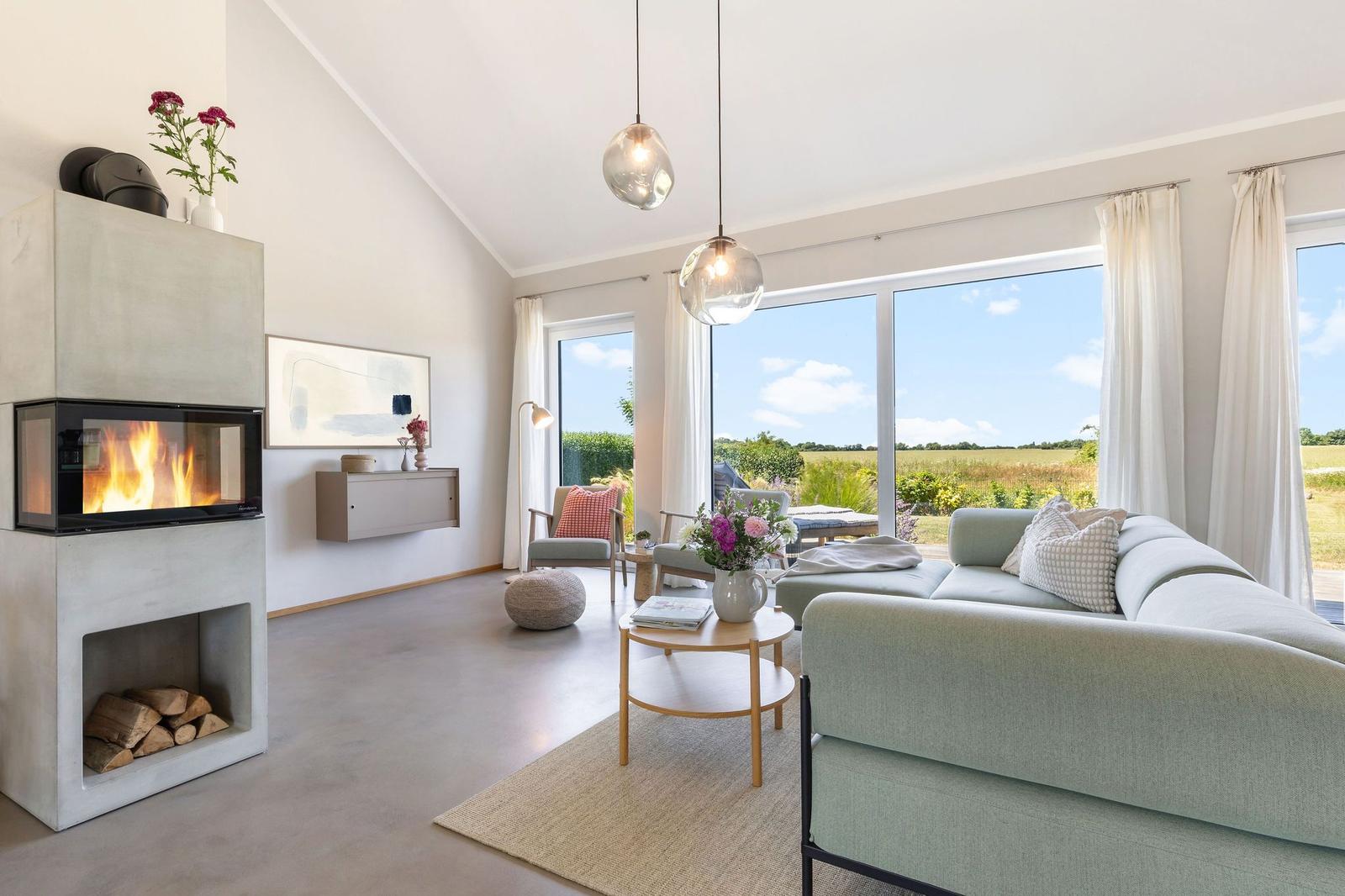 Wohnzimmer mit Kamin, Sofa und Blick auf Felder
