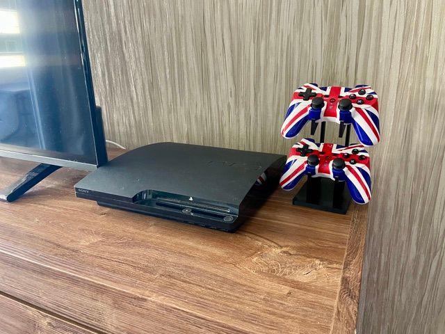 Eine PlayStation 4 und zwei Controller mit britischen Flaggenmuster stehen auf einem Holztisch.