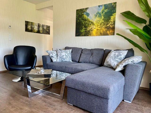 Ein Wohnzimmer mit grauem Sofa, Glas-Tisch und Wandbildern.