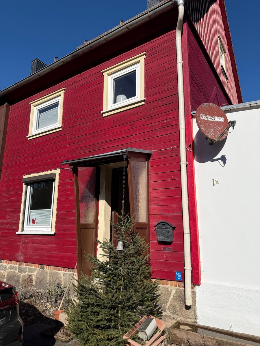Rotes Holzhaus mit Eingangstür, Fenstern und Satellitenschüssel an der Wand.