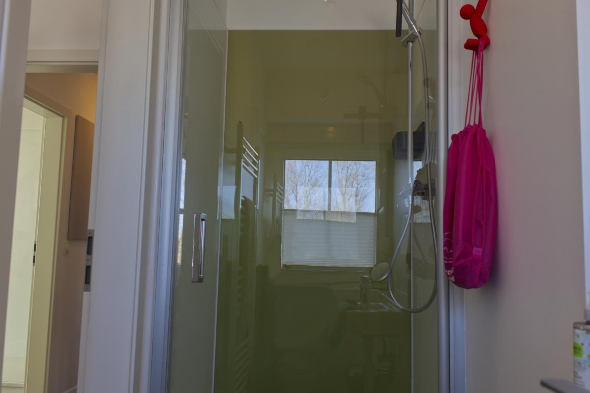 Duschbereich mit Glaswand und Fenster. Pinker Beutel hängt an der Wand.