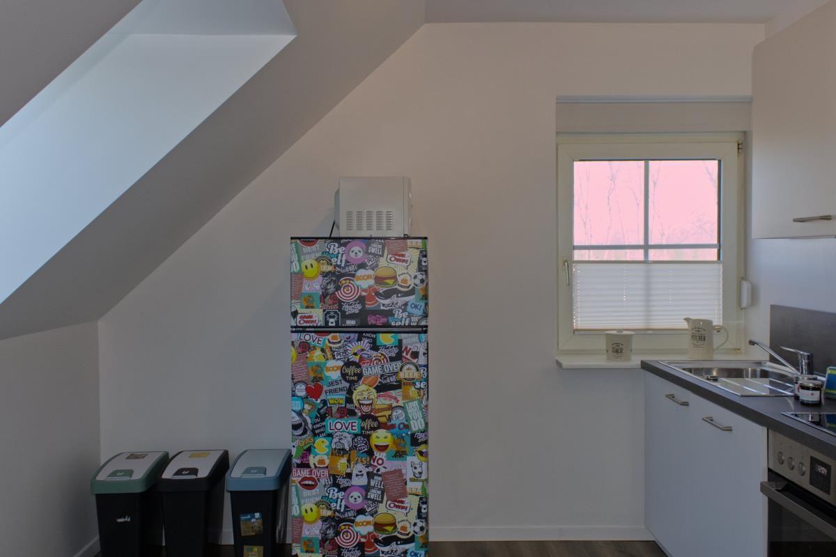 Küche mit Kühlschrank voller Aufkleber, Fenster und Abfallbehältern.