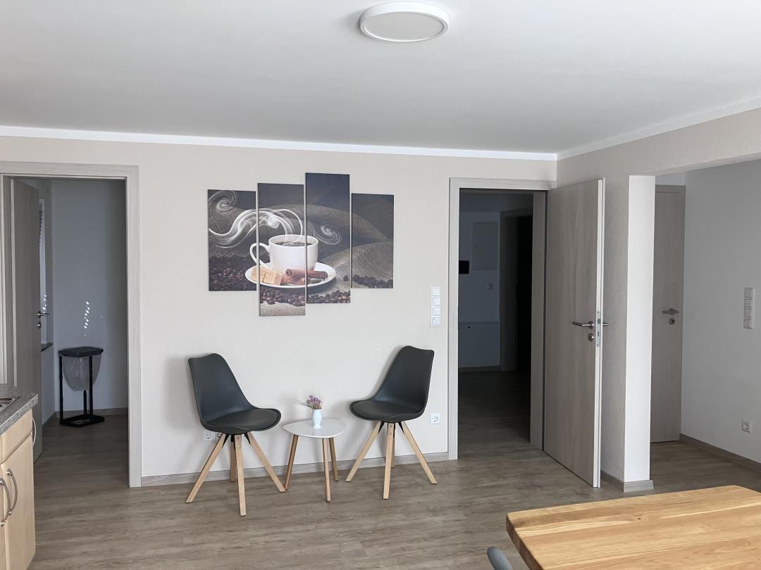 Two black chairs and a small table are in front of wall pictures.