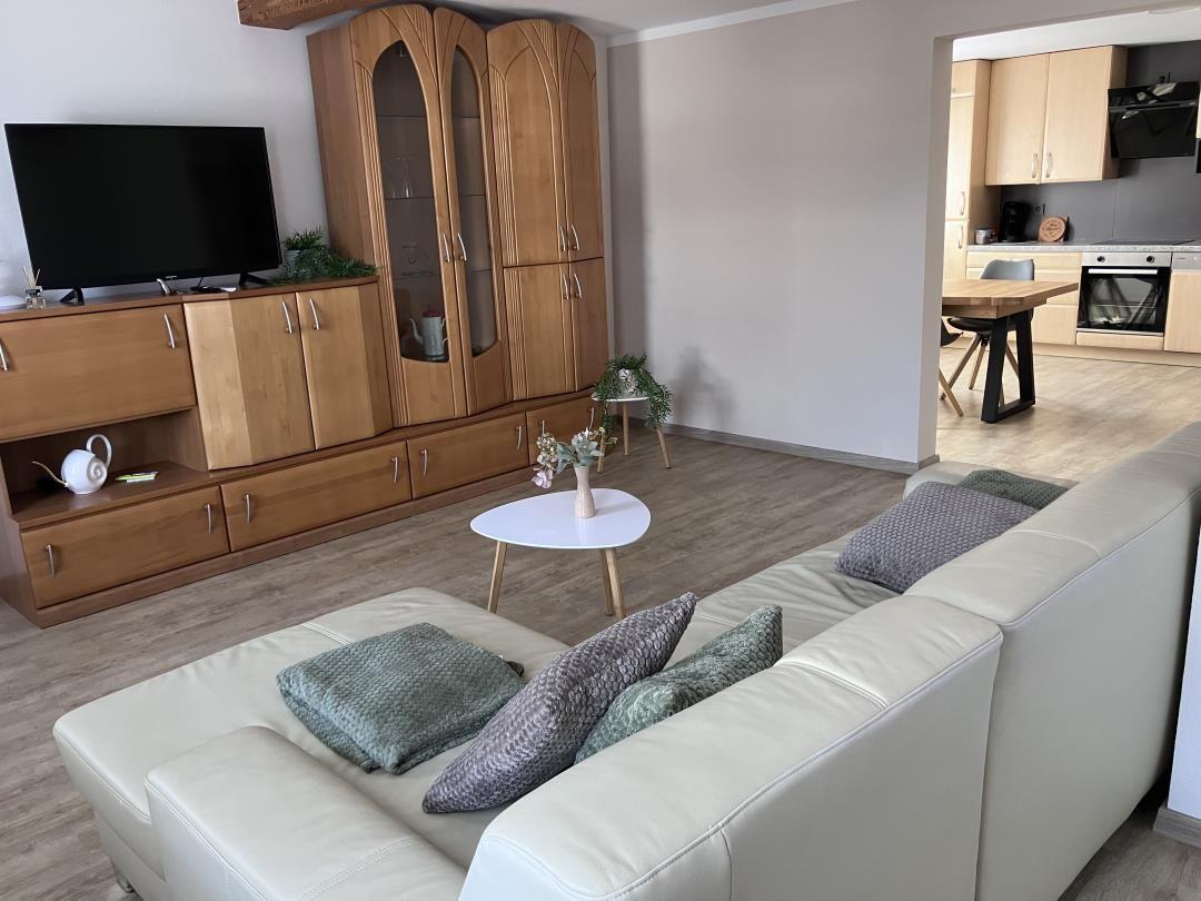 Living room with sofa, TV, and kitchen area in the background.