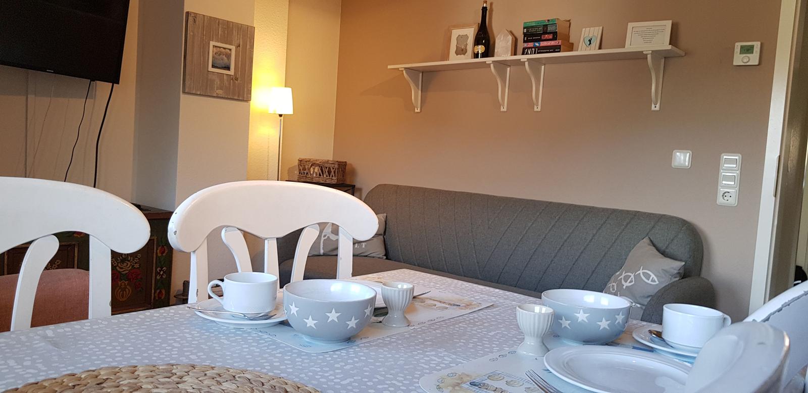 Esstisch mit weißen Stühlen und grauer Sofa-Couch im Hintergrund.