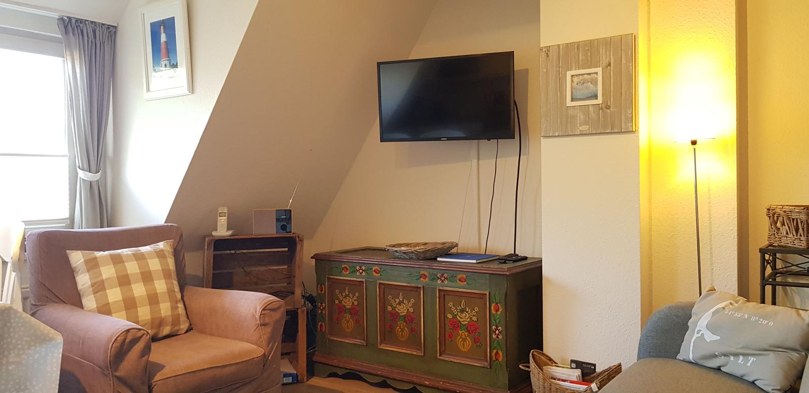 Wohnzimmer mit Sessel, Fernseher und dekorativem Schrank.