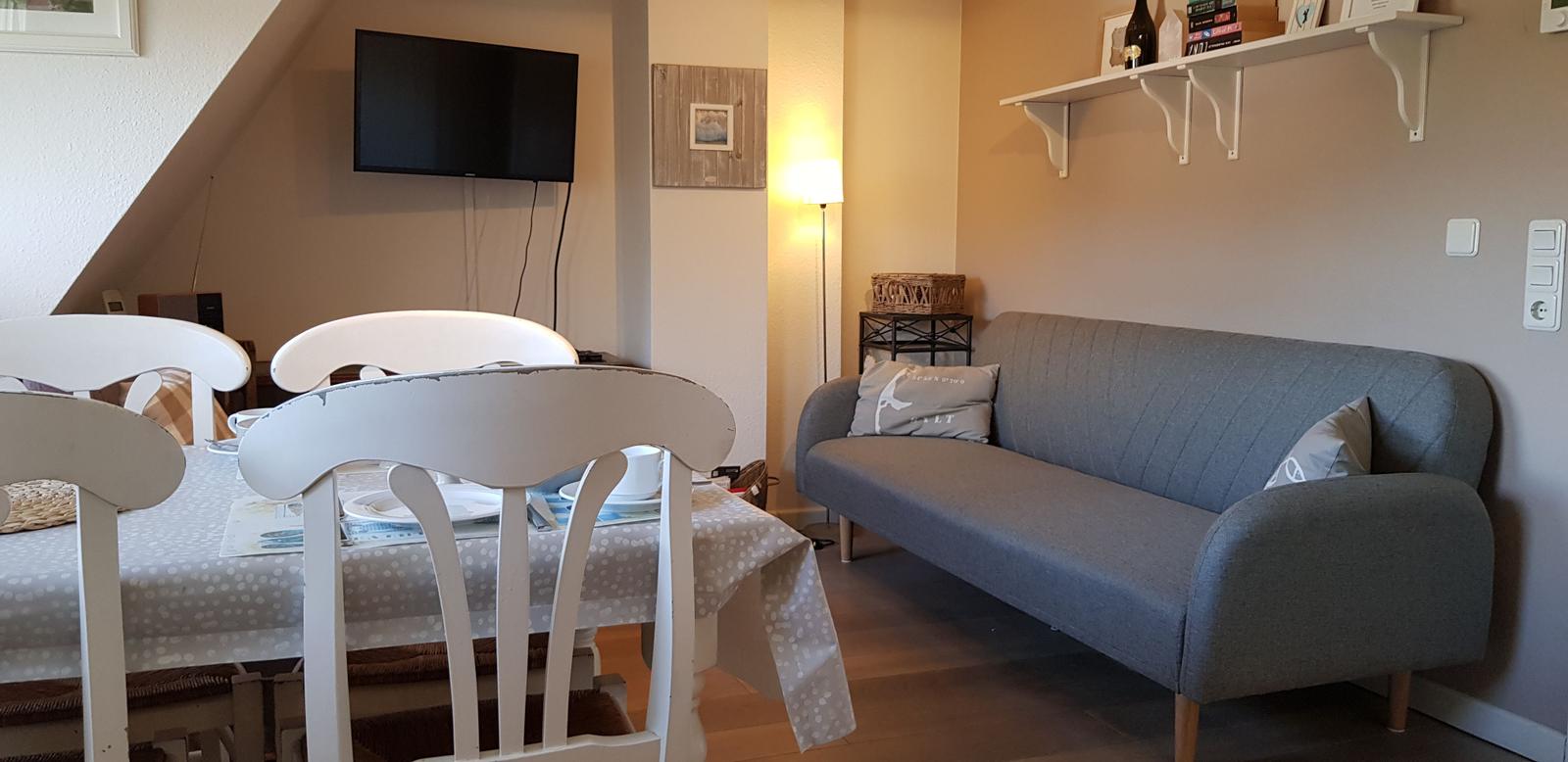 Essbereich mit Tisch und Stühlen, daneben Sofa und Fernseher an der Wand.
