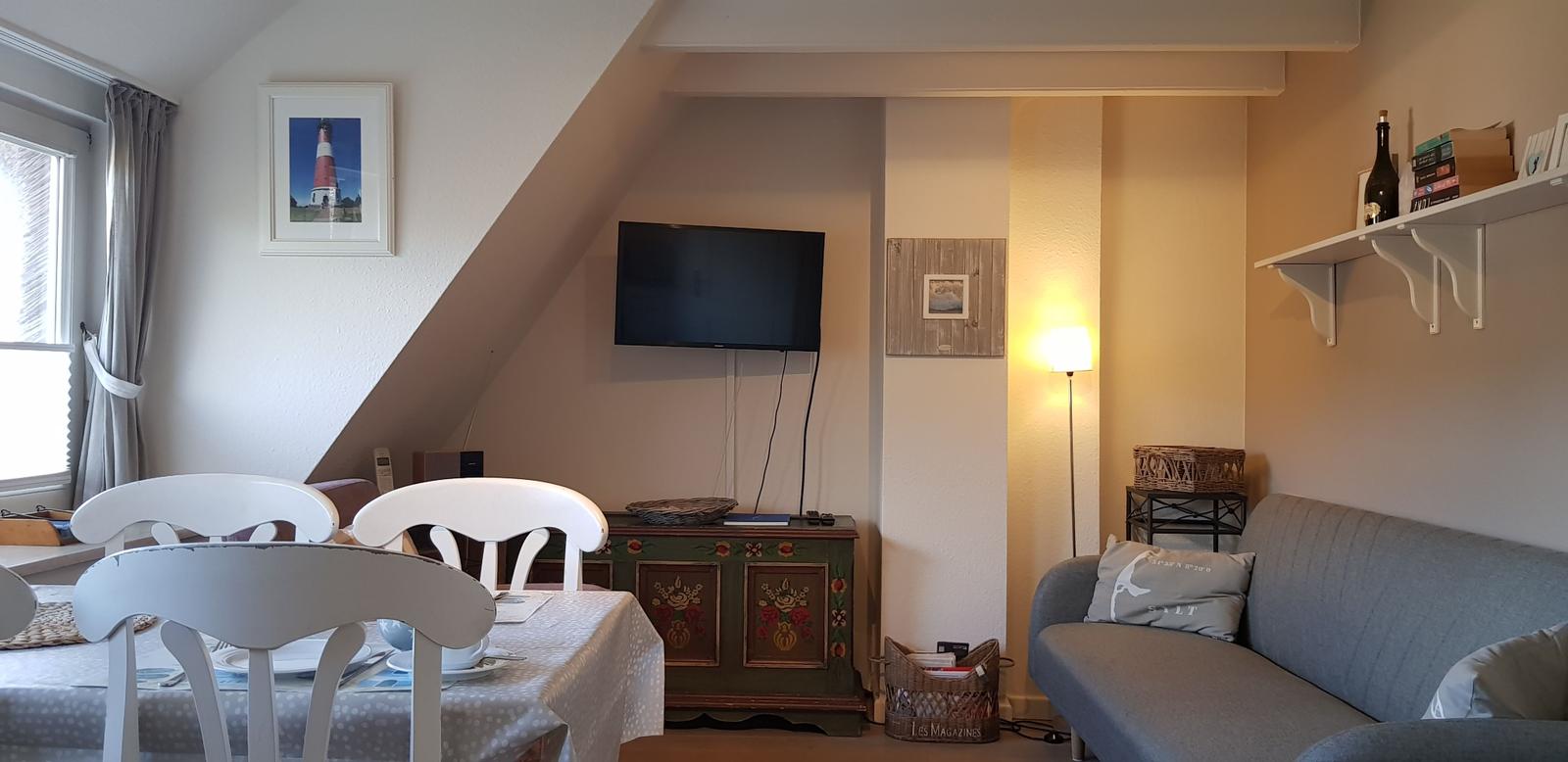 Wohn- und Essbereich mit Sofa, Tisch, Fernseher und Wandbild.