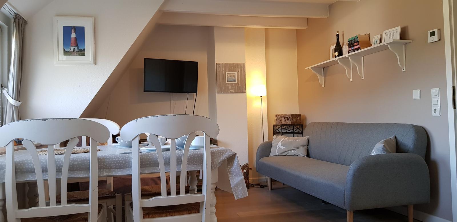 Wohn- und Essbereich mit Sofa, Esstisch und Fernseher an der Wand.