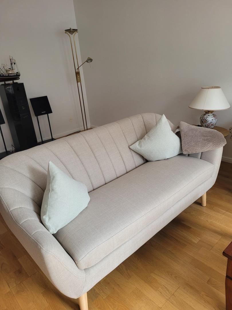 Ein hellbeiges Sofa mit Kissen auf Holzboden neben einer Stehlampe und einer Tischlampe.