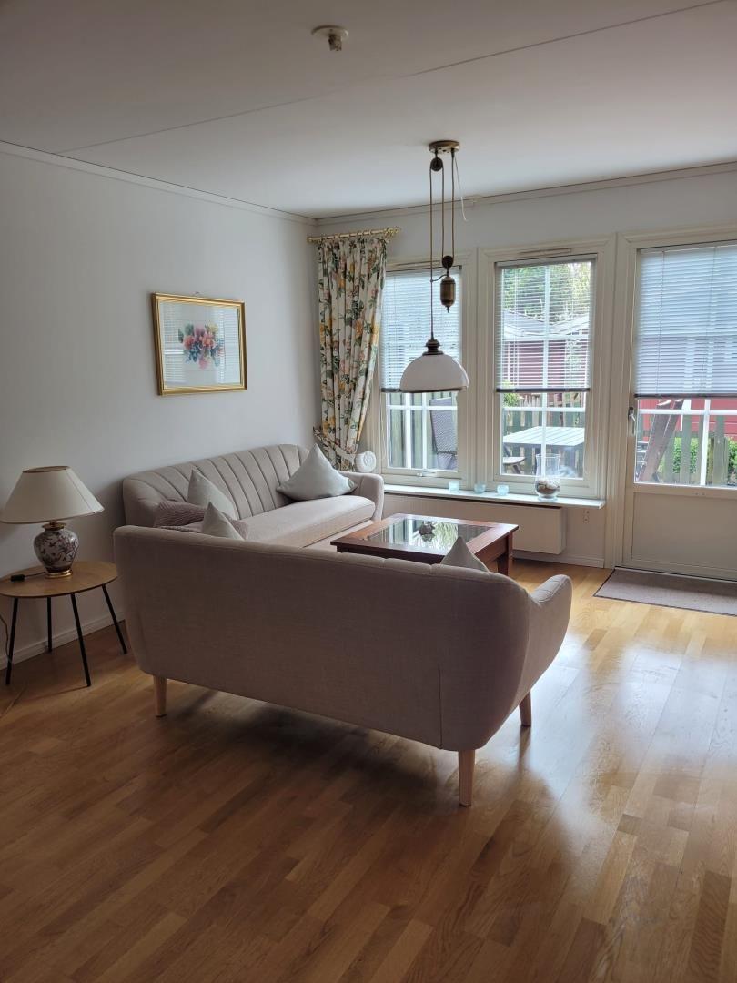 Wohnzimmer mit Sofa, Couchtisch und Holzboden. Fenster mit Jalousien und Vorhängen.