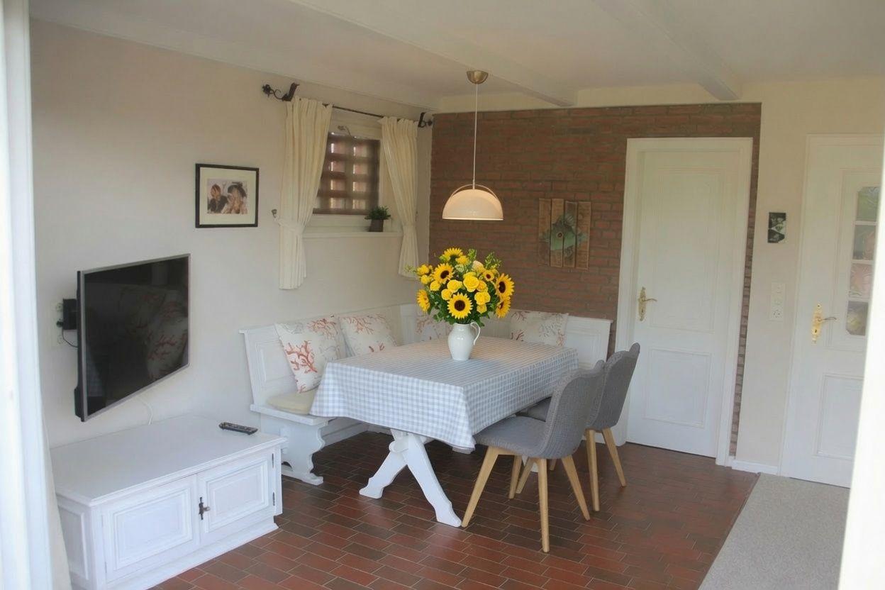 Essbereich mit Tisch, Stühlen und Blumen. Wand mit Backstein und Fenster mit Vorhängen.
