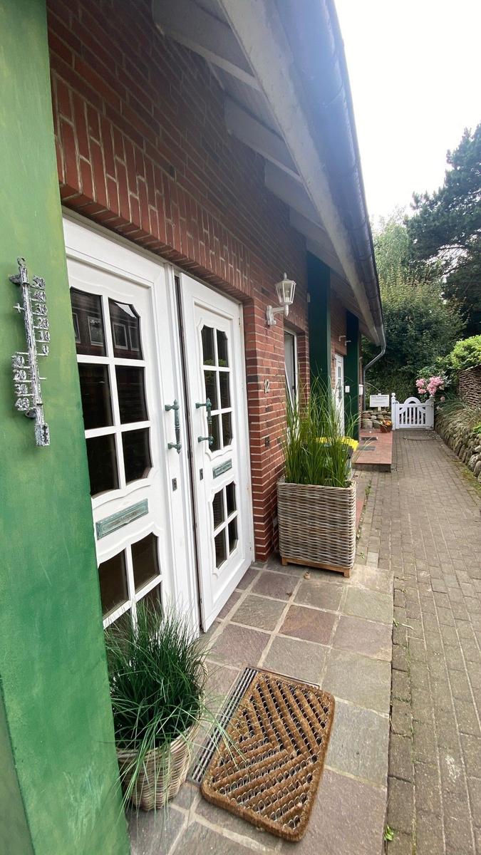 Haus mit weißen Türen, grünen Wänden und Pflanzen im Vorgarten.