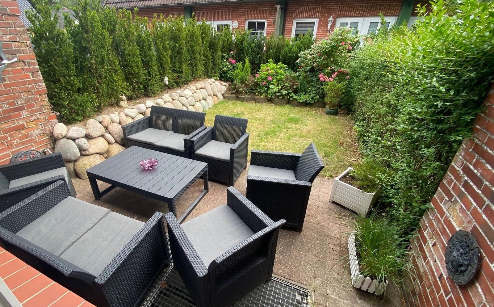 Garten mit Sitzgruppe, Rasen und Beete. Umgeben von Hecken und Steinmauer.