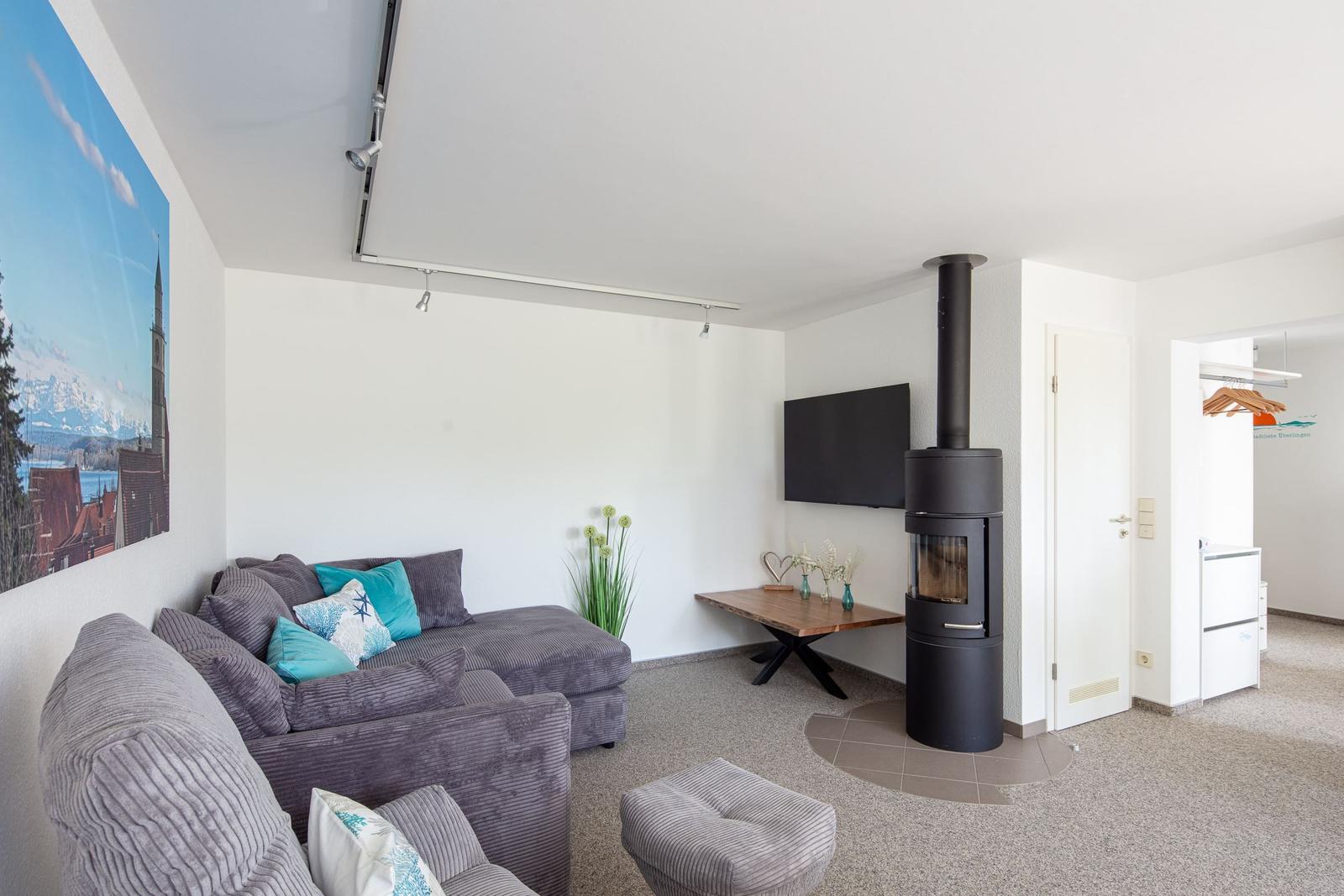 Wohnzimmer mit Sofa, Kaminofen und Fernseher.