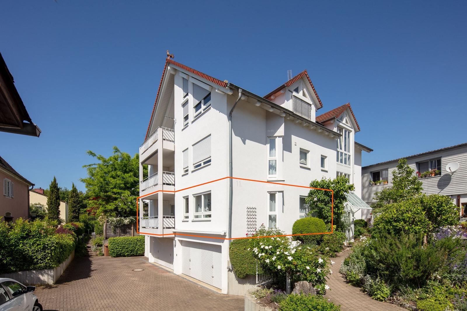 Weiße Maisonette-Wohnung mit Balkon und Gartenbereich. Modernes Design mit rotem Dachziegel.