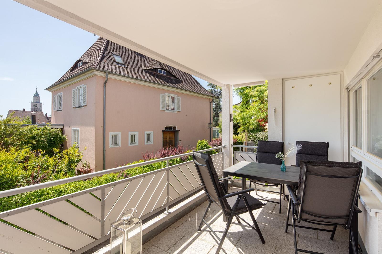Terrasse mit Tisch und Stühlen, Blick auf ein rosa Haus und einen Turm.