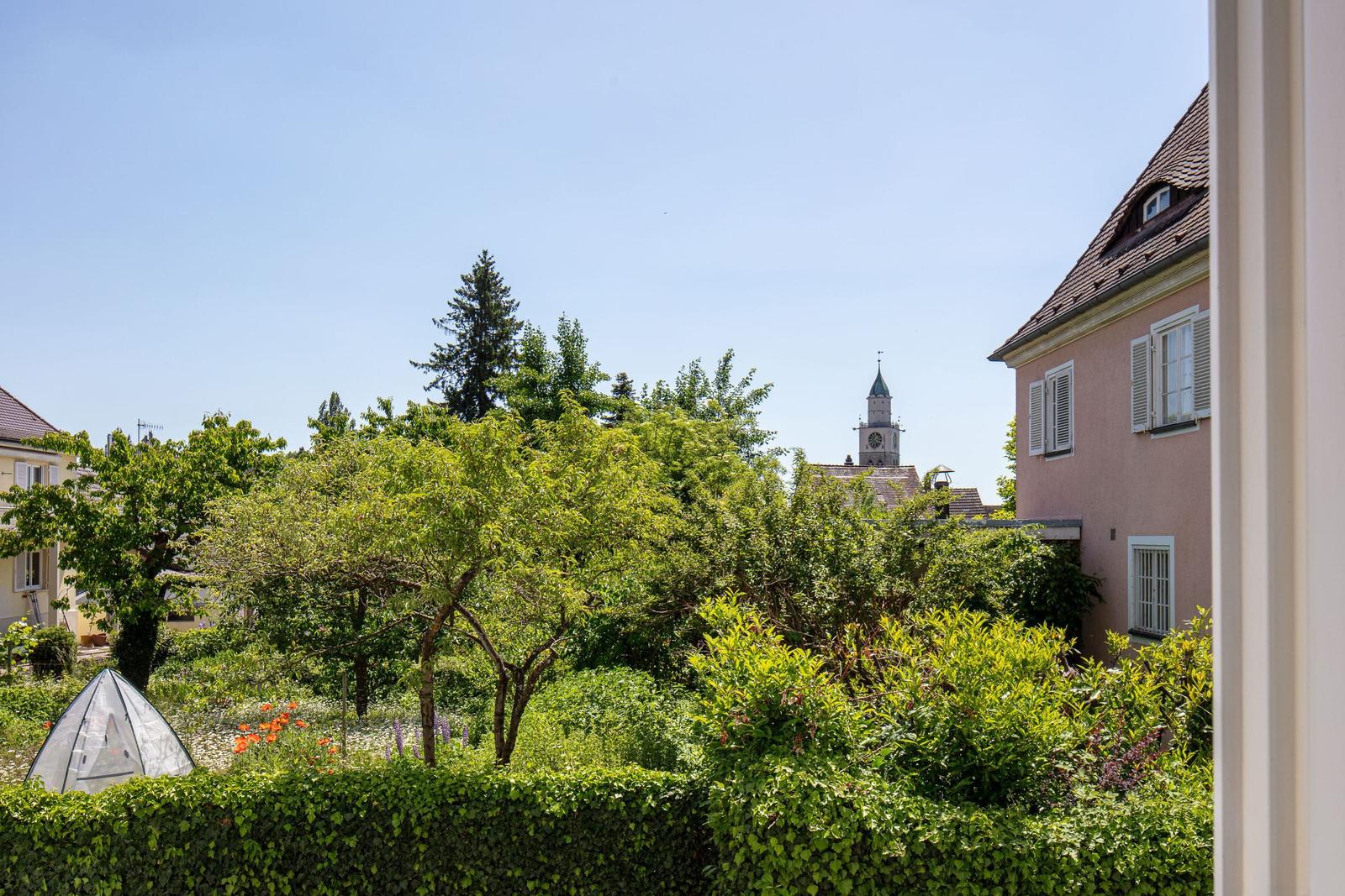 Von hier aus blickt man auf einen grünen Garten mit Bäumen und einen Kirchturm.