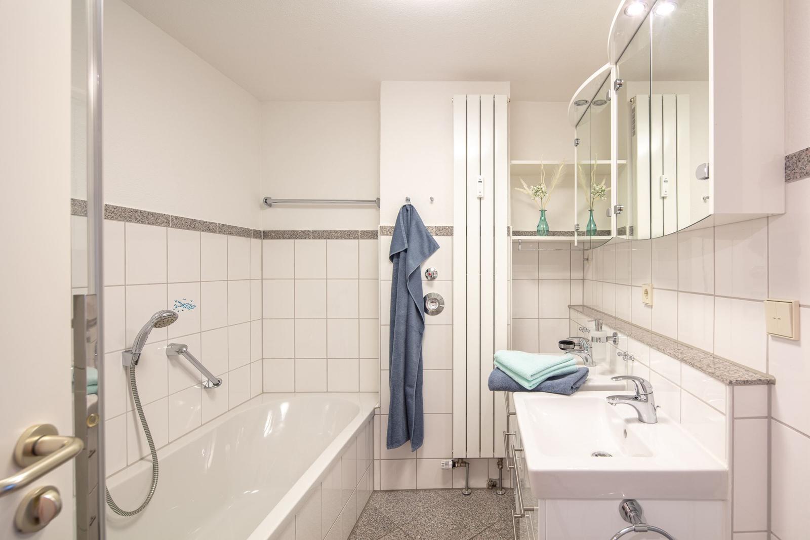 Badezimmer mit Badewanne, Duschkopf, Waschbecken und Spiegelschrank.
