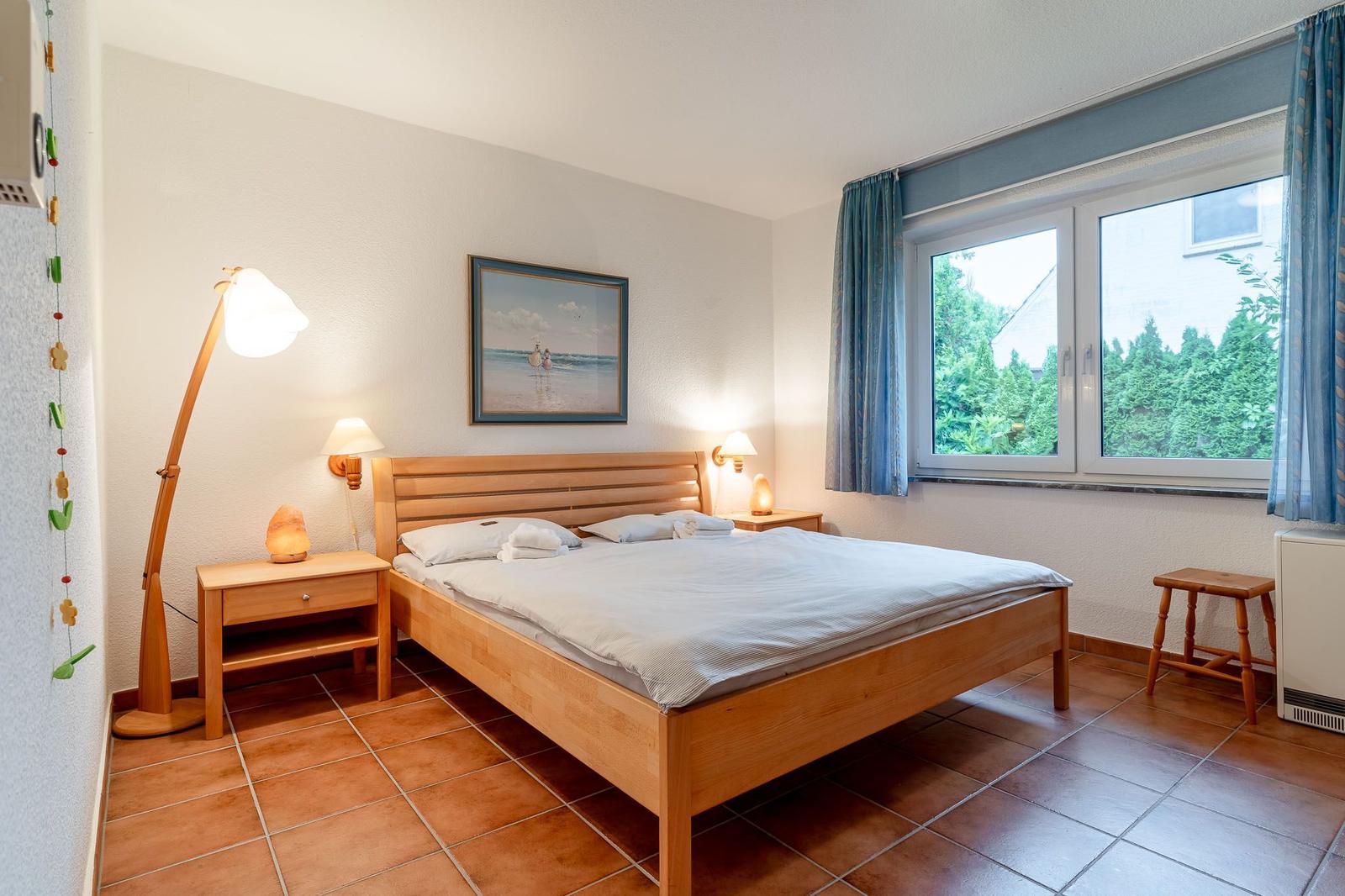 Schlafzimmer mit Holzbett, Nachttischen und Fensterblick auf Grün.