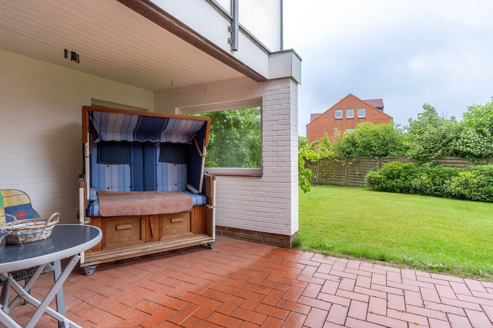 Terrasse mit Strandkorb, Tisch und Garten. Hinterhof mit Rasen und Zaun.