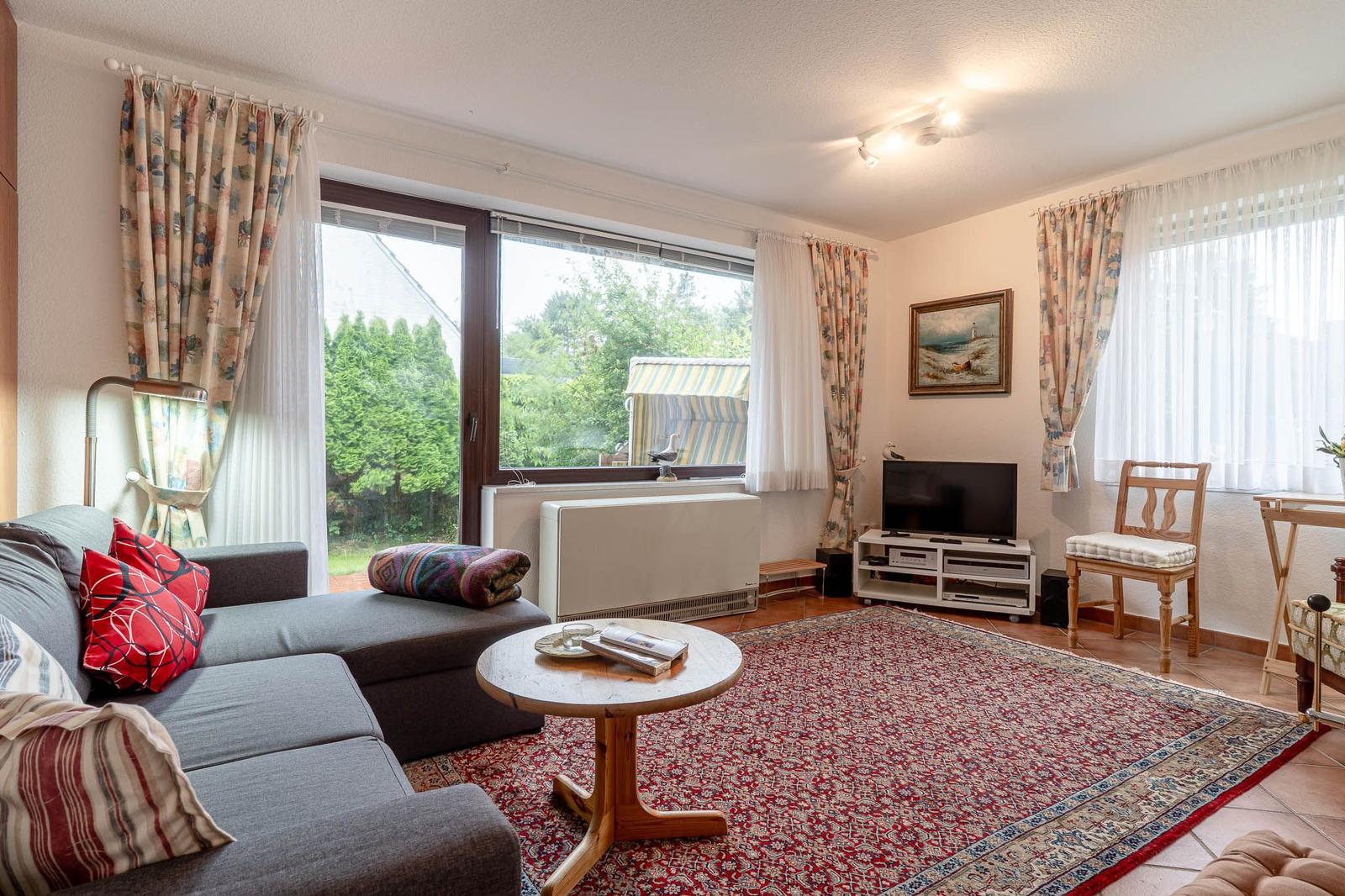Wohnzimmer mit Sofa, TV und Fenster zur grünen Außenseite.