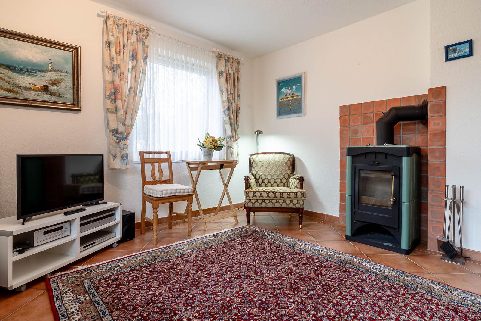 Wohnzimmer mit Holzstuhl, Sessel, Fernseher und Kaminofen.