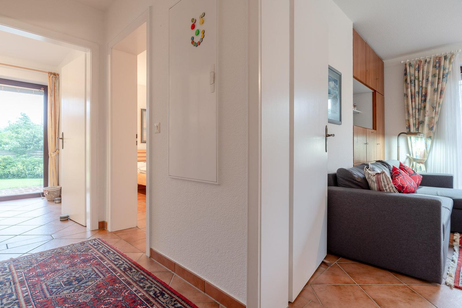 Wohnbereich mit Sofa, Tür zu Schlafzimmer und Terrasse mit Blick auf Garten.