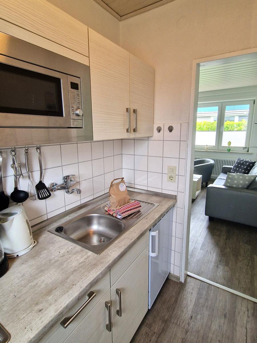 Küche mit Spüle, Mikrowelle und Arbeitsplatte. Durchgang zum Wohnzimmer mit Sofa.
