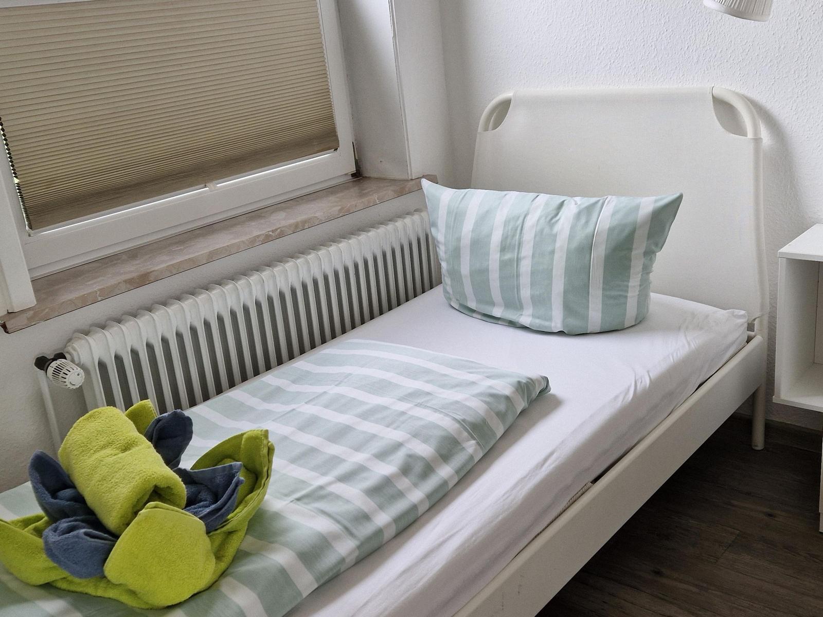 Ein Bett mit gestreifter Bettwäsche, Kissen und Handtüchern neben einem Fenster mit Jalousie.