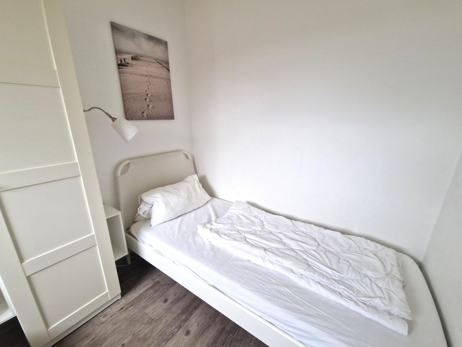 Ein Schlafzimmer mit weißem Bett, Wandbild und Schrank.