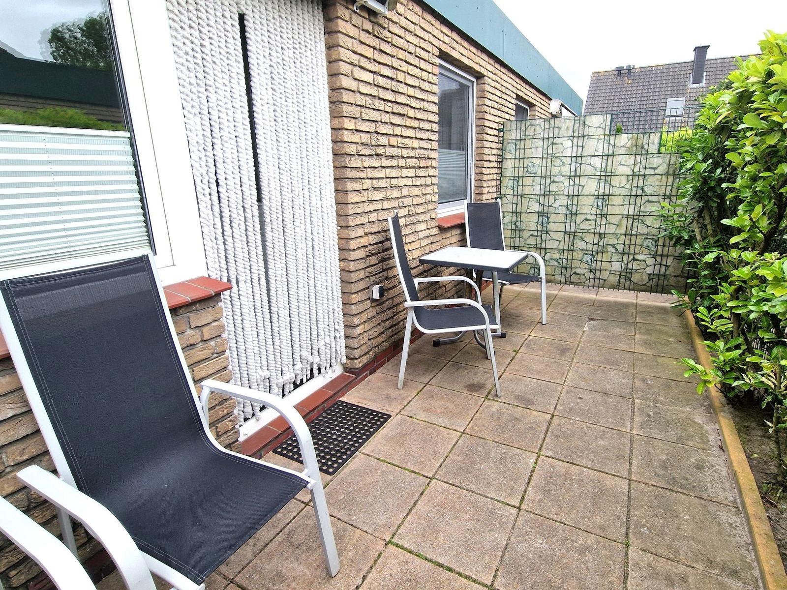 Terrasse mit zwei Stühlen und Tisch, umgeben von Steinmauer und grüner Hecke.
