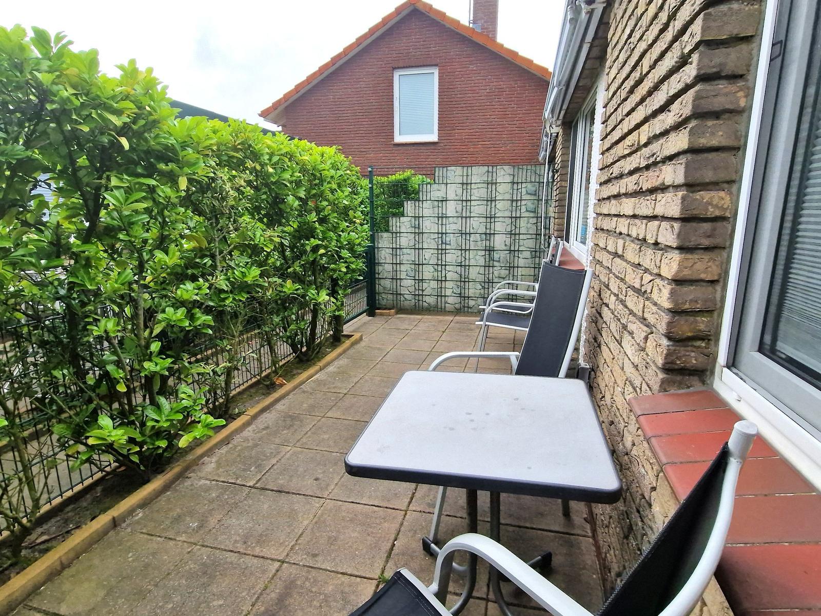 Terrasse mit Tisch und Stühlen, umgeben von Hecke und Backsteinmauer.